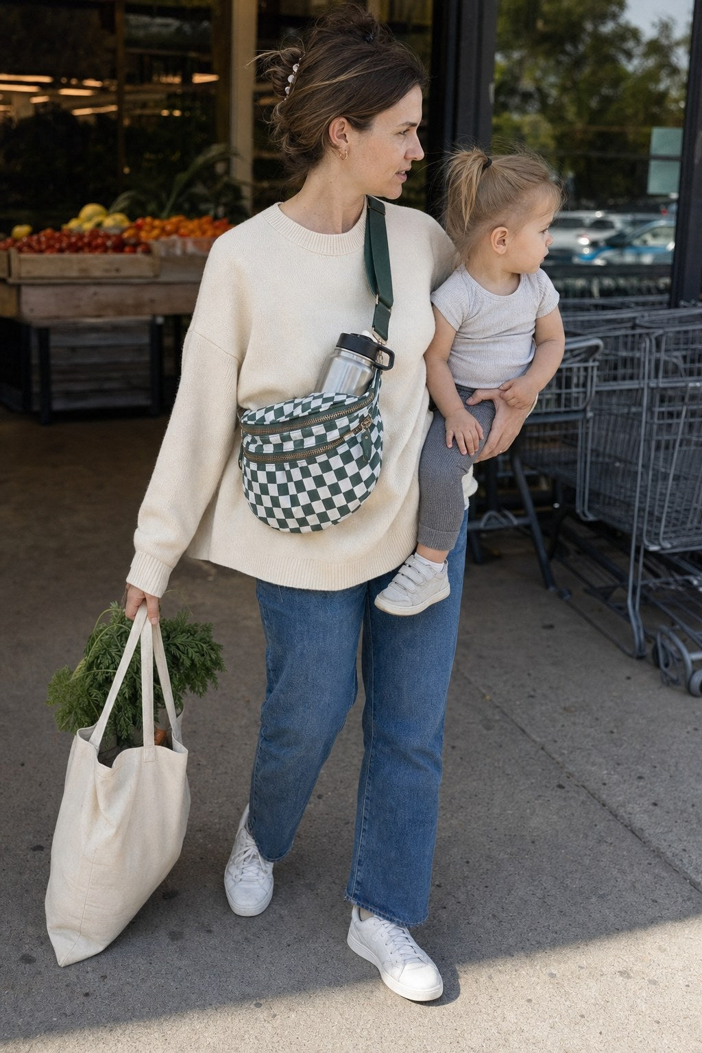 A mother carrying her toddler and groceries while wearing the CarryAll